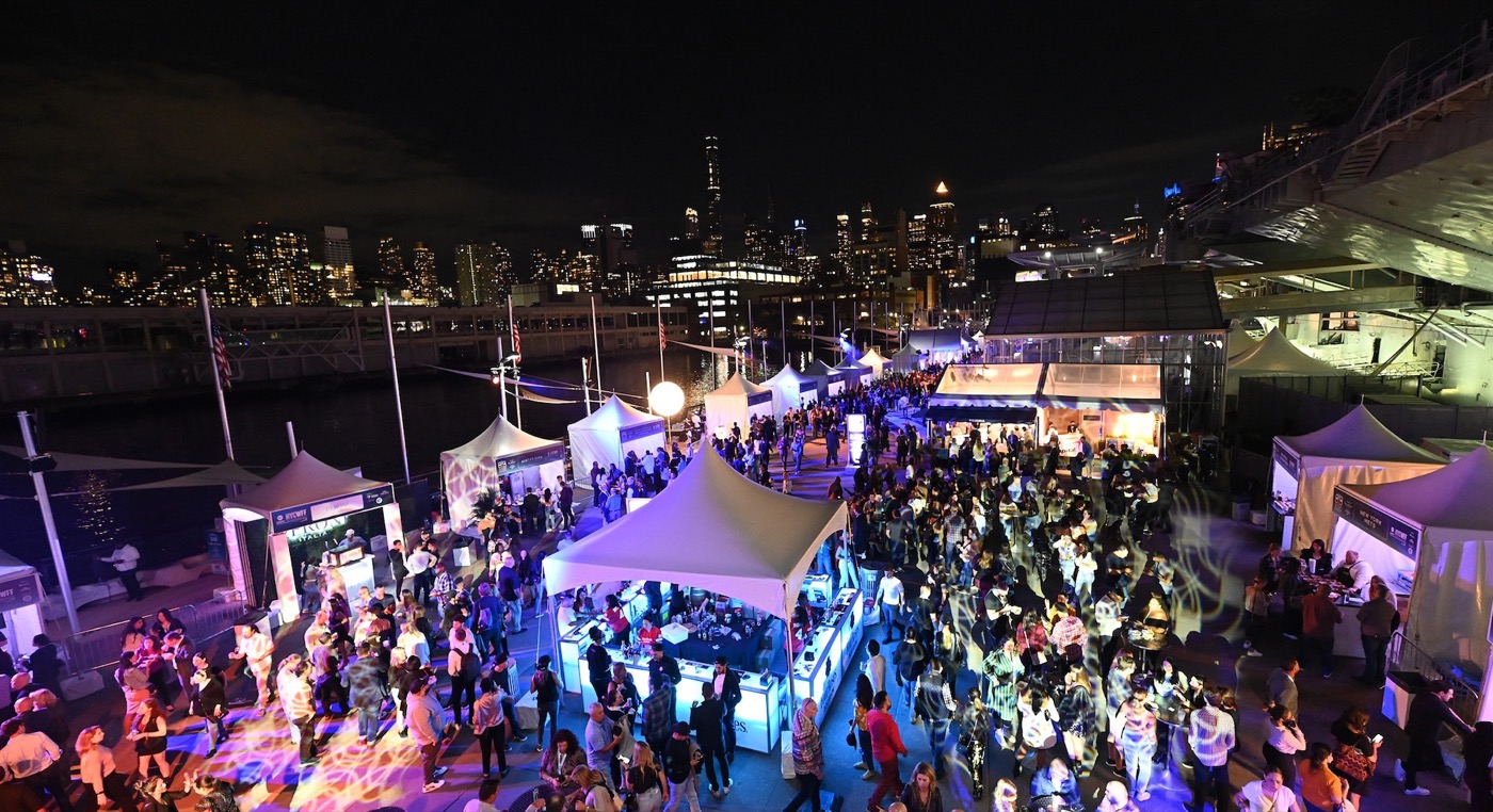 Crowds moving between lit tents on the pier at the New York City Food & Wine Festival at night