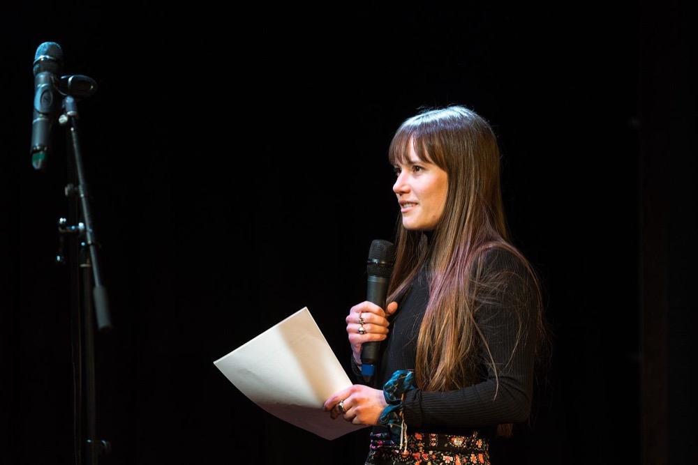 A speaker presenting with a microphone and notes under a spotlight